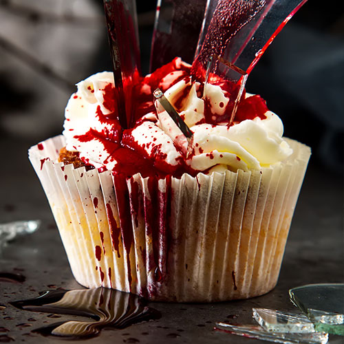 A white cupcake with broken shards of spun sugar and red berry sauce that looks like blood.