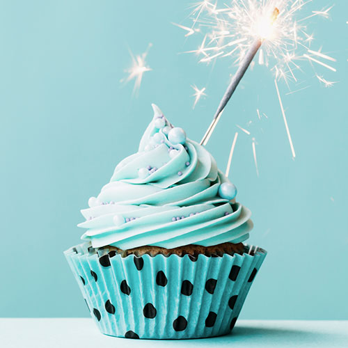 A chocolate cupcake with blue frosting in a polka-dot wrapper with a sparkler.